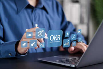 OKR Objectives, Key and Results concept. Goal setting and tracking results, Measuring results with OKRs. Businessman use laptop with OKR icons on virtual screen.