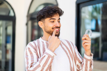 Handsome Arab man at outdoors holding invisible braces with happy expression