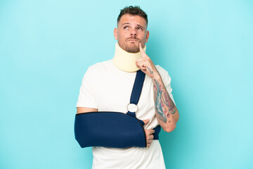 Young caucasian man wearing a sling  and neck lace isolated on blue background having doubts while...