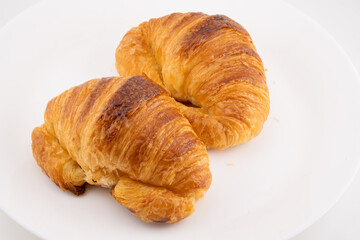 Two golden-brown croissants are positioned on a stark white surface.