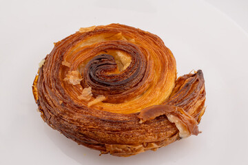 A single, golden-brown cinnamon roll, also known as a pain aux raisins or escargot pastry, is...
