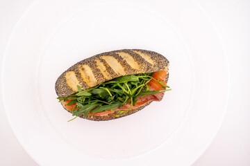 A single, appetizing smoked salmon sandwich is presented on a plain white plate.