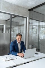 Fototapeta premium Mature Indian or Latin hispanic business man ceo manager using laptop computer typing in modern office. Middle eastern smiling senior businessman entrepreneur sitting at desk working on pc. Vertical