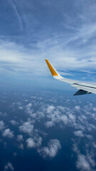 Fototapeta premium Airplane wing against a blue sky with soft clouds. Minimalist composition with large copy space, perfect for travel banners, promotions, or backgrounds, vertical photo