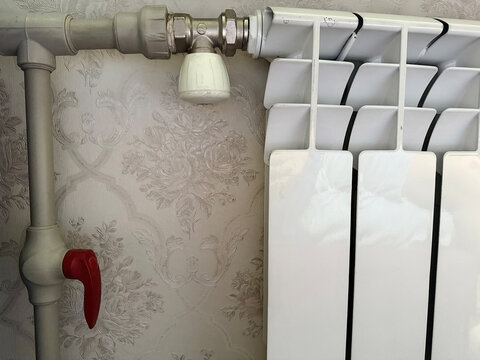 close-up of white metal radiator with manual valve on floral wallpaper background for plumbing, heating system, interior design, repair and DIY tutorial use

