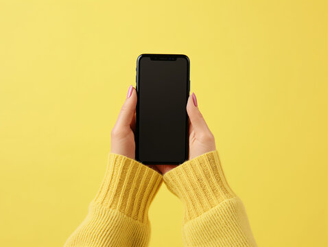 Close-up of hands holding a smartphone with blank screen for text on yellow background. financial and technology concept.