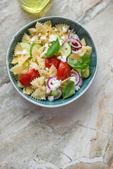 Bowl of farfalle pasta salad on a beige granite background, vertical shot with copy space, top view