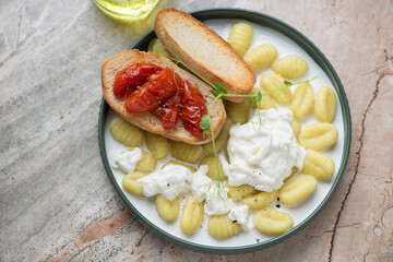 Italian gnocchi served with stracciatella and roasted tomato bruschettas, horizontal shot on a grey and roseate granite background, elevated view