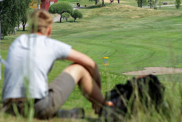 person is sitting on the hill and is following disc golf tournament