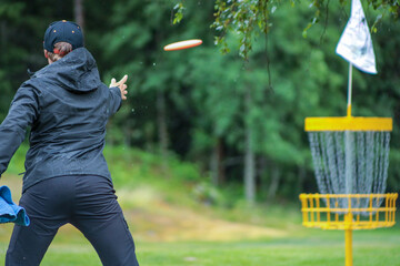 disc golf player putting to yellow basket in summer