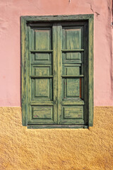 Weathered Green Wooden Window in Colorful Pink and Yellow Wall with Cracks and Texture