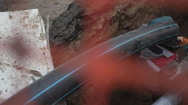 Rubber hose extends into open sewer pit. Employee of public utility installs equipment. Ensuring proper connection for drainage system