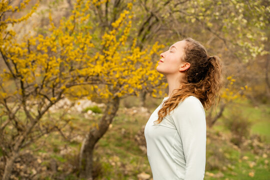 Young woman breathing in fresh air in sunlight outdoors, enjoying nature, practicing and meditating during morning with closed eyes. Mindfulness, relaxation, zen energy, wellness, mental balance