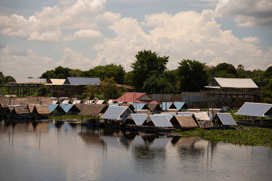 A peaceful lake village with floating huts, nestled under a bright sky and surrounded by lush greenery