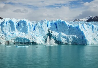 Glacier calving into turquoise water with snowy mountains behind.