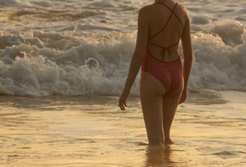 A woman in a red bikini is walking in the ocean