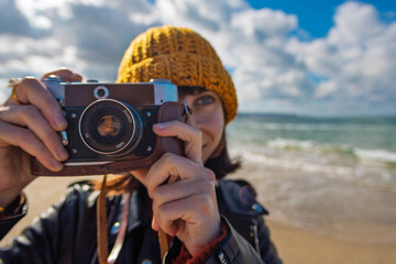 Obraz premium Woman taking photos outdoors. Young beautiful girl taking photos on camera while walking on the beach enjoying her weekend. close up.
