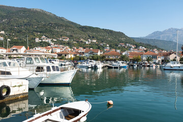 Scenic Mediterranean Marina with White Boats Docked in Coastal Town Tivat Harbor at the Foot of Green Hills and Mountains – Peaceful Summer Waterfront with Clear Blue Sky. High quality photography