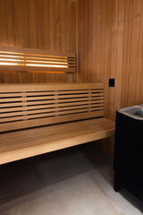 Inside of a Finnish and Nordic sauna with light wooden benches and walls, tiled floor and a black sauna heater in the corner