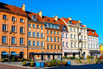 Fototapeta premium Colorful historic buildings line a sunny square in Warsaw Old Town, showcasing charming architecture and inviting cafes. Clear blue sky adds to the vibrant, picturesque atmosphere