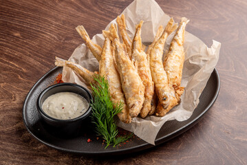 A platter of crispy fried fish served on parchment paper, accompanied by a small bowl of tangy dipping sauce. Garnished with fresh herbs, this dish offers a delightful seafood experience.