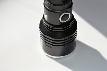 close-up photo of a black tactical flashlight white surface durable textured power button lighting...