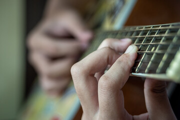 A young man is playing yellow and brown guitar in a rather dark room with lighting from the lights, during the day
