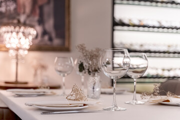 beautiful table decoration in restaurant. festive table setting in restaurant. white tablecloth on table, wine glasses, white plates, flowers in vase, candles are burning. romantic atmosphere