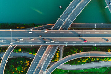Aerial view of multiple highways intersect above a calm river, surrounded by vibrant greenery.