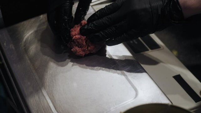 Anonymous close-up of gloved hands placing ground meat onto kitchen scales to measure a portion for a patty.