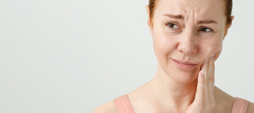 A woman suffers from severe toothache, she holds her hand to a sore tooth, her face is distorted.