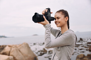 Young woman photographer with a camera on a rocky beach, demonstrating passion for photography and creativity with a serene ocean background