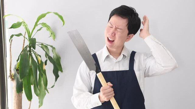 ノコギリを持ち困るエプロン姿の若い男性