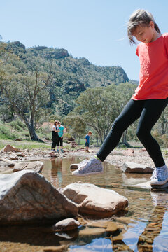 Young girl rock hopping through a creek during a bush walk