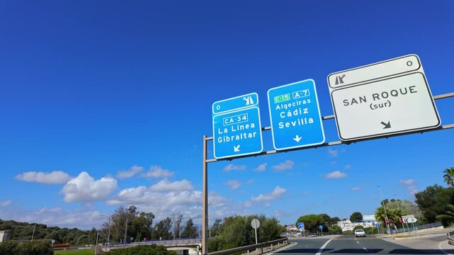 Highway signs showing directions to several cities in Andalusia such as La Linea, Gibraltar, Algeciras, Cadiz, Seville and San Roque against a blue sky