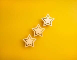 Obraz premium Shining three wooden stars ratings, isolated on yellow background, minimal style. High level of excellence quality or satisfaction, customer evaluation and review, business marketing concept.