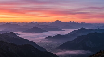 Mountain range landscape with fog in valleys under a colorful sunset sky.