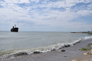 A view of a shipwreck located off the coastal shoreline, with vegetation in the foreground and calm sea