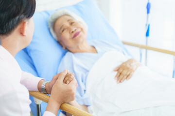Fototapeta premium Asian man visiting his elderly mother in hospital and they have a conversation together.