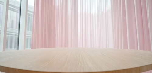 Round light wooden table with pastel pink curtains