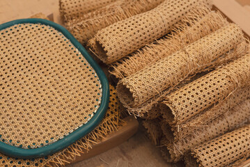 Close-up of multiple cane webbing rolls alongside a completed woven chair seat, showing natural rattan material used in traditional furniture making.