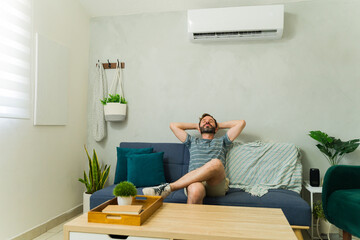 Happy Caucasian man relaxing on sofa under air conditioning unit at home