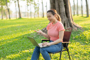 Asian woman sitting working under a tree outdoors in the evening light.
