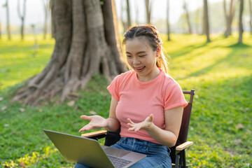 Asian woman sitting working under a tree outdoors in the evening light.