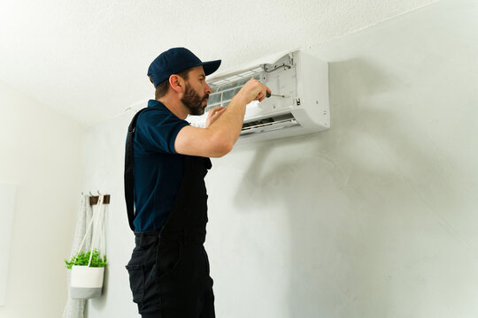 Technician repairing air conditioning unit with screwdriver