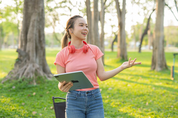 Asian woman sitting listening to music, reading a book, outdoors in nature, evening.