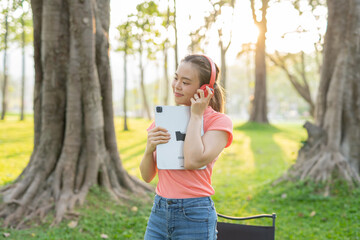 Asian woman sitting listening to music, reading a book, outdoors in nature, evening.