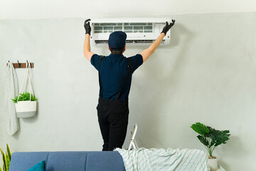 Rear view of a technician servicing an air conditioning unit in living room