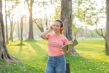 Asian woman sitting listening to music, reading a book, outdoors in nature, evening.