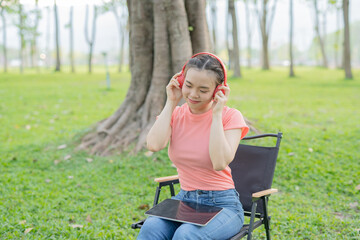 Asian woman sitting listening to music, reading a book, outdoors in nature, evening.
